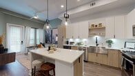 Located at 2600 N Orange Ave in Orlando, FL, this single-floor unit showcases a thoughtfully designed, modern interior with a cohesive aesthetic throughout. The open-concept kitchen serves as the centerpiece, featuring a large waterfall island with bar seating, a mix of white upper cabinetry and warm wood-toned lower cabinets, white subway tile backsplash, stainless steel appliances, a built-in wine cooler, and an under-cabinet lit countertop workspace. Pendant glass and geometric light fixtures hang above the island, adding visual interest. Wood-look flooring runs continuously throughout, unifying the living and kitchen areas.

The living room is intimate and well-lit, with large windows dressed in white linen curtains allowing ample natural light. A sliding glass door provides additional brightness and outdoor access. The bedroom is serene and spacious, featuring tall windows with layered blinds and drapes, wood flooring, and elevated ceiling height that enhances the sense of openness. The bathroom maintains the unit's modern tone with light wood vanity cabinetry, black hardware accents, a soaking tub with a dramatic black shower curtain, and pendant lighting. Overall, the space offers a clean, contemporary atmosphere with warm design details.