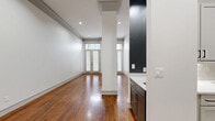 Located at 3500 Fairmount St in Dallas' vibrant Uptown neighborhood, this one-bedroom, three-bathroom residence offers a thoughtfully designed single-floor layout that maximizes both comfort and functionality. Rich hardwood flooring flows throughout the open living and dining areas, catching natural light that pours in through tall, transom-topped French doors and large windows fitted with classic plantation-style blinds. Structural columns add an architectural character to the main living space, which is further refined by elegant crown molding and recessed lighting throughout. The kitchen features dark cabinetry with gold-toned hardware and a crisp white countertop, complemented by a striking black accent wall. The bedroom is carpeted for comfort, bathed in natural light from dual windows, and connects to multiple closets for generous storage. Three bathrooms serve the residence, including one finished with luxurious marble-style tile flooring and walls, a soaking tub, and warm wood cabinetry with modern fixtures. A dedicated laundry area adds everyday convenience. The overall ambiance is clean, contemporary, and polished, blending classic architectural detailing with modern finishes throughout.