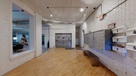 This single-floor space is a thoughtfully converted industrial building that retains its original character while offering a range of functional amenities. The welcoming lobby features whitewashed brick walls, warm hardwood floors, a white-painted wood-plank ceiling with recessed lighting, a wall of resident mailboxes, and a metal bench — setting an industrial-chic tone throughout.

Beyond the entry, a generously sized common lounge area showcases exposed ductwork, structural steel beams, and original hardwood floors. The space is furnished with large leather sofas and armchairs arranged around a coffee table, complemented by indoor greenery, wall art, and a bookshelf — creating a relaxed, community-oriented atmosphere.

An expansive open area with soaring ceilings, exposed steel columns, and a mezzanine-level walkway above provides flexible space currently used as a recreation room, complete with a foosball table. The raw, loft-like aesthetic is enhanced by exposed wood-joist ceilings and painted brick walls.

A dedicated fitness room offers hardwood floors and pendant lighting, housing cardio machines, a weight station, and a ping-pong table. Additional utility spaces and corridors connect the various zones seamlessly, maintaining the building's cohesive industrial design language throughout.