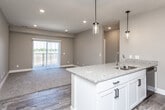 This single-floor residence offers a thoughtfully designed open-concept layout that seamlessly connects the kitchen, dining, and living areas. The kitchen is a standout feature, showcasing white shaker-style cabinetry, granite-look countertops, a large center island with a stainless steel sink, and stainless steel appliances including a refrigerator, range, and microwave. Stylish pendant lights hang above the island, adding a modern touch to the space. The adjacent living area is finished with plush carpeting and benefits from an abundance of natural light streaming in through a sliding glass door that opens to a private balcony overlooking open outdoor scenery. Durable wood-look vinyl flooring runs throughout the kitchen and hallways, creating a clean contrast with the carpeted living and bedroom spaces. The bedrooms are generously sized, each featuring neutral tones, soft carpet, and windows that frame pleasant outdoor views. The bathrooms are finished with granite-look vanity tops, white cabinetry, and wood-look vinyl flooring; one features a shower-tub combo while another includes a walk-in closet for added convenience. A textured ceiling, recessed lighting, and a neutral warm-gray color palette lend a cohesive, contemporary feel throughout.