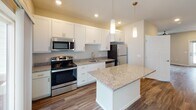 This two-story home offers a well-designed layout with contemporary finishes throughout. The kitchen serves as a central highlight, featuring white shaker cabinetry, granite countertops, a central island with pendant lighting overhead, and a full suite of stainless steel appliances including a range, microwave, dishwasher, and refrigerator. Wood-style plank flooring runs through the kitchen and main living areas, adding warmth and continuity. A sliding glass door in the kitchen/living area connects the interior to an outdoor patio, allowing natural light to flow in.

The bedrooms are carpeted and naturally lit by windows that overlook the surrounding neighborhood. Ceiling fans are present in select rooms. The bathrooms are finished with granite-topped white vanities and wood-style flooring; one bathroom includes a tub/shower combination, while another features a stacked washer and dryer unit, providing convenient in-unit laundry. Neutral wall tones and clean white trim throughout the home create a cohesive, move-in-ready aesthetic that is both functional and modern in character.