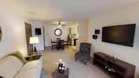 This single-floor residence offers a thoughtfully designed layout that balances comfort and functionality across its key living areas. The living room serves as the heart of the home, featuring plush carpeting, a large sliding glass door with vertical blinds that invites natural light, and ample space for relaxed seating arrangements. A ceiling fan overhead adds to the room's comfort. Adjacent to the living area, a dedicated dining space accommodates a round table and chairs beneath its own ceiling fan, with a charming round mirror adding a decorative touch to the wall nearby. Two interior doors provide convenient access to closets or storage. The galley-style kitchen is efficiently organized with light wood cabinetry, a double basin sink, a dishwasher, electric range, refrigerator, and a microwave, all set against tile flooring and sage-toned walls. The primary bedroom is generously sized, carpeted, and features a ceiling fan, a window with a view of lush greenery, and a closet. A versatile second room with soft blue walls offers flexible use as a home office or guest space. The bathroom is bright and clean, featuring a vanity with under-cabinet storage, a large mirror, and well-appointed fixtures. Throughout the residence, warm neutral tones and carpet flooring create a cohesive, welcoming ambiance.