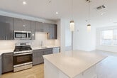 This thoughtfully designed 2-bedroom, 2-bathroom residence at 620 Bloomfield Avenue in Bloomfield, NJ offers a clean, modern aesthetic across a well-proportioned single-floor layout. Light hardwood flooring flows throughout the living areas and bedrooms, complementing the crisp white walls and contemporary finishes.

The open-concept kitchen is a standout feature, showcasing sleek gray high-gloss cabinetry, a classic white subway tile backsplash, stainless steel appliances including a gas range and French door refrigerator, and a generous quartz-topped island with pendant lighting above — seamlessly connecting to the living area.

The living room is bright and airy, benefiting from large windows with roller shades that frame views of the surrounding Bloomfield streetscape. The spacious primary bedroom continues the light-filled theme with oversized windows and ample room to configure comfortably. The second bedroom is equally well-lit with its own window and natural light. Both bedrooms are served by dedicated closets, including a walk-in closet with wire shelving for organized storage.

Both bathrooms are finished in a modern, all-white palette with quartz vanity countertops, large mirrors, glass-enclosed showers, and tile flooring. One bathroom also features a stacked in-unit washer and dryer, adding everyday convenience. A hallway connects the layout efficiently, completing this polished and functional residence.