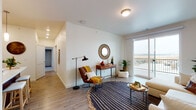 Located at 2120 W A St in Pasco, Washington, this thoughtfully designed single-floor residence offers a clean, modern aesthetic throughout. A welcoming entry hallway with wood-look flooring leads into an open-concept living space bathed in natural light. The living room is anchored by large sliding glass doors that open to a private balcony, offering expansive views of the surrounding landscape — a standout feature of the unit.

The kitchen is a functional and stylish centerpiece, showcasing rich dark-stained cabinetry, white subway tile backsplash, light countertops, and black appliances including a range, microwave, and refrigerator. A peninsula with pendant lighting and bar seating adds a casual dining option and enhances the open flow between kitchen and living areas.

The bedrooms feature plush wall-to-wall carpeting and well-sized windows that fill each room with natural light. The primary bedroom includes a sliding barn-style door, adding a modern design touch. The bathroom is clean and practical, featuring dark wood vanity cabinetry, a walk-in shower, and wood-look vinyl flooring consistent with the rest of the home.

Throughout the unit, a neutral color palette, recessed lighting, and consistent wood-look flooring create a cohesive and contemporary living environment.