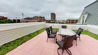 This single-floor space offers a thoughtfully designed layout with a standout feature: a private rooftop terrace that delivers panoramic views of the surrounding urban skyline. The terrace is finished with warm-toned tile pavers and bordered by a low privacy wall, beyond which a lush green sedum border adds a natural contrast to the cityscape. Wicker dining chairs and a tile-top table furnish the outdoor area, creating a comfortable setting for al fresco dining or relaxation. The surrounding cityscape, with its mix of mid-rise buildings and open sky, provides a dynamic backdrop.

Inside, the interiors reflect a clean and understated aesthetic. Soft neutral tones—warm cream and cool gray—carry throughout the walls and trim, creating a calm and cohesive atmosphere. White panel doors with classic raised molding detail add a traditional architectural touch. The hallways are finished with plush carpet and bright white baseboards, maintaining a polished appearance. Storage is well-considered, with closets equipped with shelving and hanging rods supported by white bracket hardware. The overall design balances functional living with an inviting, well-maintained character suited to urban living.