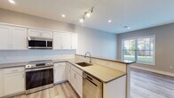 Located at 57 W Merritt Blvd in Fishkill, NY, this contemporary single-floor residence offers a thoughtfully designed layout with modern finishes throughout. The kitchen serves as a centerpiece of the home, boasting white shaker-style cabinetry, a subway tile backsplash, quartz countertops, and a full suite of stainless steel appliances including a range, built-in microwave, refrigerator, and dishwasher. A peninsula with an undermount sink and breakfast bar seating opens seamlessly to the living area, enhancing the open-concept flow. Light hardwood-style flooring extends throughout the main living spaces, complementing the neutral warm-toned walls and crisp white trim. The living area is generously proportioned, with multiple windows inviting abundant natural light and views of the surrounding greenery. The bedrooms are well-sized and bright, each featuring windows and easy-care flooring. The bathrooms are finished with a clean, modern aesthetic—one featuring marble-look tile flooring, a vanity with white countertop, and a tiled tub-shower combination, while a second bath offers a similarly refined design. Recessed and track lighting throughout ensures well-lit interiors at every hour of the day.