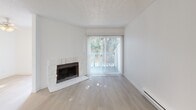 Located in Tukwila, WA, this single-floor, one-bedroom unit offers a clean and functional layout with a bright, neutral aesthetic throughout. The living area features light hardwood-style flooring, crisp white walls, and a textured ceiling, creating an airy and open feel. A standout feature is the wood-burning fireplace with a white stone surround, accompanied by a sliding glass door that floods the room with natural light and opens to an outdoor balcony area. A ceiling fan adds comfort to the adjacent dining or flex space, which connects seamlessly to the rest of the unit. The galley-style kitchen is efficiently designed with white cabinetry on both sides, light countertops, a stainless steel sink, white appliances including a range and refrigerator, and ample upper and lower cabinet storage. The layout maximizes every inch of the space. The bedroom is carpeted for warmth and comfort, offering a generously sized sliding closet with built-in shelving. A large window provides natural light and views of the surrounding exterior. The unit maintains a consistent, clean design language throughout, with white trim, neutral tones, and practical finishes that make it easy to personalize.