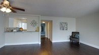 This single-floor residence offers a thoughtfully designed layout that promotes an open, connected living experience. The main living area is anchored by rich, dark hardwood flooring that extends throughout, providing a warm and elegant foundation for the space. Crisp white walls and a textured ceiling complement the neutral palette, creating a clean and inviting ambiance.

A partial wall with a pass-through counter separates the living area from the kitchen, maintaining an open feel while defining each functional zone. The kitchen benefits from natural light streaming through a window, brightening the space and offering a welcoming atmosphere. Decorative touches, including ornamental wall art and accent vases, add character and warmth to the interior.

A central hallway connects the living area to the additional rooms beyond, suggesting a practical and efficient floor plan. The corridor leads to what appears to be bedrooms and additional living spaces, all maintaining the consistent design language of the home. A ceiling fan is partially visible, indicating thoughtful climate considerations throughout.

Overall, this residence balances functionality with aesthetic appeal, featuring consistent finishes, a cohesive color scheme, and a layout designed for comfortable everyday living.