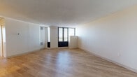 This single-floor unit at 186 State Street in Springfield, Massachusetts, offers a clean, modern interior defined by light hardwood flooring that extends throughout every room. The open living area is generously proportioned, featuring large floor-to-ceiling windows framed in dark trim that allow substantial natural light to fill the space while offering views of the surrounding cityscape. HVAC vents integrated into the walls provide year-round climate control.

The layout transitions smoothly from the living area into a dedicated kitchen, which is equipped with rich, dark-stained wood cabinetry extending along the full length of the wall. White appliances, including a gas range and dishwasher, are complemented by light countertops and a single-basin sink, creating a functional and organized workspace.

The bedroom is a well-proportioned room with its own large window, continuing the hardwood flooring found throughout the unit. A closet with built-in shelving provides practical storage. The bathroom is finished with white subway tile surrounding the tub-shower combination, a dark wood vanity with a white countertop, a medicine cabinet mirror, and chrome fixtures, all set on matching hardwood flooring. The overall ambiance is clean, bright, and functional.