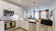 This thoughtfully designed single-floor residence offers a seamless blend of style and functionality across its well-utilized layout. The open-concept kitchen and living area serves as the heart of the home, featuring a sleek white kitchen outfitted with shaker-style cabinetry, white subway tile backsplash, stainless steel appliances, and a peninsula island with bar seating illuminated by modern pendant lighting. Light wood-style flooring flows throughout, enhancing the bright, airy atmosphere. The living area provides generous space for relaxation and entertaining, with large windows allowing ample natural light.

The bedroom offers a comfortable and private retreat, complemented by a spacious walk-in closet with built-in shelving and hanging systems. A second closet provides additional storage convenience. Both bathrooms are well-appointed, with one featuring a soaking tub with subway tile surround and a vanity with ample counter space. A dedicated office with carpet flooring, a ceiling fan, and a window with drapes creates an ideal work-from-home environment. The in-unit laundry area houses a full-size front-loading washer and dryer. Neutral tones, recessed lighting, and ceiling fans throughout contribute to a clean, modern aesthetic.