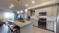 This thoughtfully designed single-floor residence offers a cohesive blend of modern finishes and functional layout. The open-concept kitchen serves as the heart of the home, showcasing granite countertop surfaces, a large central island with bar seating, gray shaker-style cabinetry, a white subway tile backsplash, and a full suite of stainless steel appliances including a refrigerator, range, microwave, and dishwasher. Pendant lighting overhead adds warmth and definition to the space.

The living area is generously sized, featuring wood-look flooring, a ceiling fan, and a sliding glass door that opens to a private balcony with outdoor views. The bedroom accommodations are comfortable and well-proportioned, with wood-look flooring, neutral wall tones, and ample natural light from window treatments.

Two bathrooms serve the residence. The primary bathroom includes a walk-in closet with wire shelving and a glass-enclosed standing shower. The secondary bathroom features a granite-topped vanity with gray shaker cabinetry, a large mirror, and a tub-shower combination. Both bathrooms continue the wood-look flooring found throughout the residence, creating a consistent aesthetic. Recessed lighting and tasteful artwork complement the space's contemporary, welcoming ambiance.