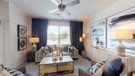 This single-story 1-bedroom, 1-bathroom residence combines modern design with functional living across a well-planned layout. The living room serves as the heart of the home, featuring a ceiling fan, large windows dressed with dramatic floor-to-ceiling dark drapes, and abundant natural light with outdoor views. The space accommodates both a comfortable seating area and a dedicated dining nook nestled in a bright bay window corner, ideal for everyday meals. The kitchen is outfitted with stainless steel appliances, granite countertops, a deep undermount sink, subway tile backsplash, and two-toned cabinetry — all complemented by light wood-style flooring. A dedicated laundry area with a full-size washer and dryer is conveniently accessible from the kitchen. The bedroom offers a serene retreat with plush carpet, natural light from large windows, a statement geometric accent wall, and access to a generous walk-in closet. The bathroom features a granite-topped vanity with ample storage, a framed mirror, and a full tub-shower combination with clean white tile surround. Throughout the residence, a cohesive neutral palette with warm wood accents creates an inviting and contemporary ambiance.