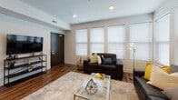 Located at 708 S 6th St in Champaign, IL, this modern single-floor unit offers a thoughtfully designed layout ideal for comfortable living. The kitchen is a standout feature, showcasing dark espresso cabinetry, a mosaic tile backsplash, white countertops, stainless steel appliances including a refrigerator, range, microwave, and dishwasher, and a breakfast bar with seating — all set atop warm wood-look flooring. The open living area provides ample natural light through a bank of windows fitted with blinds, creating a bright and welcoming atmosphere. Wood-look flooring continues throughout the main living space, complementing the clean, neutral wall tones. The unit includes multiple carpeted bedrooms, each offering a quiet and comfortable retreat. One bedroom features a window with natural light and space for a desk, making it well-suited for studying or remote work. Two bathrooms serve the unit: one with a glass-enclosed shower stall and dark vanity cabinetry, and another with a shower-tub combination, large vanity mirror, and access to a walk-in closet. Light tile flooring in the bathrooms contrasts elegantly with the dark cabinetry. Light wood-tone interior doors add a modern touch throughout the space.