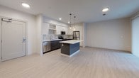 Located at 200 Presidential in Woburn, Massachusetts, this thoughtfully designed single-floor residence offers a clean, modern aesthetic throughout. The open-concept kitchen and living area serves as the heart of the space, featuring light hardwood-style flooring that extends seamlessly across the main living zone. The kitchen is outfitted with two-tone cabinetry — dark lower cabinets paired with crisp white uppers — complemented by marble-style quartz countertops, a tile backsplash, and a full suite of stainless steel appliances including a range, over-the-range microwave, refrigerator, and dishwasher. A central island with pendant lighting above adds both functionality and visual interest. The living area is bright and airy, benefiting from natural light through a large sliding glass door that opens to an outdoor balcony. The bedroom is finished with plush carpeting, a generously sized window with exterior views, and access to a spacious walk-in closet equipped with wire shelving for organized storage. The bathroom maintains the residence's modern character with large-format white tile flooring, a wood-toned vanity with white countertop, and a clean, minimalist layout. Recessed lighting throughout keeps the space well-lit and contemporary.