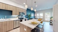 Located in Portland, OR, this thoughtfully designed 2-bedroom, 1-bathroom unit offers a modern open-concept layout that maximizes every inch of its compact footprint. The combined kitchen and living area serves as the heart of the space, where light wood-toned cabinetry, stainless steel appliances, and a white quartz waterfall island create a sleek, functional kitchen. A bold teal accent wall anchors the area, adding a vibrant pop of color against the light hardwood-style flooring. Pendant lighting over the island enhances the contemporary aesthetic. The living room flows naturally from the kitchen, featuring large windows and a sliding door that open to a private balcony, inviting ample natural light and outdoor views. The primary bedroom is a well-proportioned retreat with a walk-in closet equipped with built-in shelving. The second bedroom is bright and cozy, with a window overlooking the surrounding neighborhood. The bathroom is cleanly finished with warm wood vanity cabinetry, a white countertop, and a shower-tub combination with light wood-style flooring. Clean lines and a neutral palette throughout create a cohesive, contemporary ambiance.