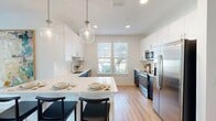 This thoughtfully designed 2-bedroom, 2-bathroom residence spans a single floor and offers a cohesive, modern aesthetic throughout. Light wood-tone flooring runs continuously across the home, complementing the bright white walls and creating a warm, airy atmosphere.

The open-concept kitchen is a standout feature, showcasing two-tone cabinetry with crisp white uppers and dark lower cabinets, white quartz countertops, a subway tile backsplash, and stainless steel appliances including a refrigerator, range, microwave, and dishwasher. A kitchen island with seating provides additional prep and dining space, while pendant lighting adds a refined touch. Natural light pours in through a window overlooking greenery.

The combined dining and living area is generously proportioned, with the dining space anchored by large windows and a sliding glass door leading to a balcony. The living room features a ceiling fan, arched decorative wall details, and ample room for entertaining.

Two well-lit hallways connect the bedrooms and bathrooms, with closet storage conveniently located along the way. The primary bedroom is a comfortable retreat with a ceiling fan, large windows with sheer drapery, and direct access to a bathroom featuring a glass-enclosed walk-in shower with tile surround. The second bedroom mirrors the same clean, bright design. Both bathrooms maintain the home's modern finishes with wood-look flooring and clean fixtures.
