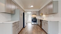 This well-maintained two-floor residential unit offers a bright, neutral interior with a clean, modern aesthetic throughout. The galley-style kitchen is a standout feature, equipped with stainless steel appliances including a range, dishwasher, and refrigerator. Light wood-toned cabinetry with sleek bar-pull hardware lines both walls, complemented by white quartz countertops and a classic subway tile backsplash. Wood-look flooring runs through the kitchen and hallway areas, adding warmth and durability. A built-in floor-to-ceiling storage cabinet in the main hallway provides convenient organizational space, while recessed lighting illuminates the corridor leading between floors. The spacious living area features plush wall-to-wall carpeting, large sliding glass doors dressed with vertical blinds for natural light and outdoor access, and a stylish chandelier overhead. Additional windows with horizontal blinds further brighten the space. Carpeted bedrooms are generously sized with neutral white walls and ceiling vents for climate control. The bathroom includes a wide vanity with light wood cabinetry, white countertop, a large mirror, and a combined tub and shower enclosure. A staircase with carpeted treads connects the two floors, completing this functional and move-in-ready home.