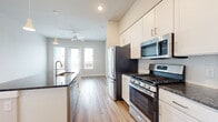 Located in Austin, TX (78717), this thoughtfully designed one-bedroom, one-bathroom residence offers a functional and modern living experience. The open-concept kitchen is a standout feature, showcasing white shaker cabinetry, dark granite countertops, a central island with additional seating space, and a full suite of stainless steel appliances including a gas range, built-in microwave, and refrigerator. A tile backsplash and pendant lighting complete the polished look. Wood-style luxury vinyl plank flooring runs throughout the main living areas, adding warmth and continuity to the space. The living area benefits from natural light through a glass door and flanking windows, and is outfitted with a ceiling fan overhead. The bedroom features plush carpet, a large window with outdoor views, and direct access to the bathroom. The bathroom includes white cabinetry with granite countertops and tile flooring, and connects to a dedicated walk-in closet with built-in shelving and hanging rods. A dedicated entrance and additional closet storage round out the practical elements of this well-appointed Austin residence.