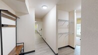 Located at 19500 14 Mile Rd in Big Rapids, Michigan, this single-floor unit offers seven bedrooms and four bathrooms, designed to accommodate a shared living arrangement with efficiency and comfort. The open kitchen and living area serves as the social hub of the unit, featuring white cabinetry, laminate countertops, a full suite of appliances including a range and refrigerator, and a breakfast bar with seating — seamlessly flowing into a carpeted living room area. Each bedroom is thoughtfully designed for individual use, with select rooms featuring a built-in kitchenette complete with a mini-fridge and microwave, making them highly functional private spaces. Closets throughout are equipped with wire shelving systems for organized storage. The four bathrooms are finished with wood-look tile flooring, vanities with laminate countertops, and shower-tub combinations with decorative curtains. A dedicated in-unit laundry room houses a full-size washer and dryer on durable luxury vinyl plank flooring. Wide hallways connect the rooms throughout, and the light, neutral color palette lends a clean and airy feel to the entire space. This unit is well-suited for student housing or group living near Ferris State University.
