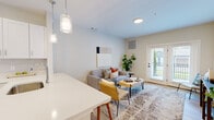 Located in Boylston, MA, this thoughtfully designed one-bedroom, one-bathroom residence offers a cohesive and modern living experience across a single, efficiently organized floor. The open-concept layout connects the kitchen and living room, creating a seamless flow ideal for both everyday living and entertaining. The kitchen is outfitted with crisp white shaker cabinetry, stainless steel appliances including a refrigerator, range, and over-the-range microwave, complemented by white quartz countertops and light wood-tone flooring that extends throughout the space. The living area is bright and inviting, featuring neutral-toned walls, recessed and pendant lighting, and French doors that open to a private outdoor balcony with views of the surrounding greenery. The generously sized bedroom accommodates a full suite of furniture, benefits from a large window that brings in natural light, and includes access to a walk-in closet. The bathroom is finished in a clean, minimalist style with large-format light tile flooring, a white vanity with ample storage, and a frameless glass shower. A hallway connects the living areas to the private spaces, contributing to an efficient and comfortable floor plan throughout.