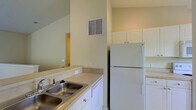 Located at 3900 Suffolk Dr in Dublin, Ohio, this single-floor residence offers a well-designed open-concept layout that maximizes both functionality and comfort. The living area is generously proportioned, featuring plush wall-to-wall carpeting and vaulted ceilings that lend an airy, open feel to the space. Recessed lighting illuminates the interior, complemented by natural light streaming in through a large sliding glass door that provides direct access to the outdoors and offers views of surrounding greenery.

The kitchen is seamlessly integrated into the main living space via a peninsula-style breakfast bar, creating a natural transition between cooking and entertaining areas. It is outfitted with white cabinetry, including upper cabinets that extend toward the ceiling for ample storage. A full-size refrigerator, dishwasher, and a double-basin stainless steel sink round out the kitchen's practical amenities. Neutral-toned countertops and a ventilation vent overhead complete the efficient layout.

Throughout the home, warm beige and cream tones on the walls create a bright, welcoming atmosphere. The single-floor design ensures easy accessibility and a cohesive flow between all areas of the residence, making it a practical and comfortable living space in the Dublin, Ohio community.