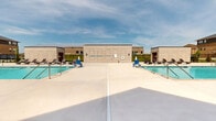 Located at 2290 SE Waco Pl in Waukee, Iowa, this outdoor amenity area serves as a central recreational hub for the surrounding residential community. The space is defined by two generously sized swimming pools with clear, blue water, each flanked by wide concrete sun decks equipped with wicker chaise lounge chairs ideal for relaxing under the open Iowa sky. The pool area is enclosed by a sleek, black wrought-iron fence with decorative stone pillar accents, providing both security and visual continuity with the surrounding multi-story residential buildings, which feature a combination of brick, stone, and board-and-batten siding. A dedicated clubhouse or amenity building adjoins the pool deck, offering direct access between indoor and outdoor spaces. Manicured green lawns and young ornamental plantings are visible beyond the fencing, contributing to a well-maintained and inviting atmosphere. A secure chemical storage room, constructed from matching light-colored masonry block and accessed via heavy steel double doors with appropriate hazard signage, is integrated into the facility's infrastructure. The overall design reflects a modern, community-oriented aesthetic that prioritizes outdoor recreation, safety, and attractive landscaping throughout the grounds.
