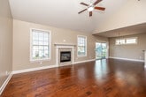 This two-story home is designed with a thoughtful layout that balances open communal spaces with practical private areas. The main living area immediately draws attention with its soaring vaulted ceiling, ceiling fan, and rich hardwood flooring that extends throughout the main level. A tile-surround fireplace with a classic white mantel serves as the focal point of the living room, flanked by multiple windows that flood the space with natural light. Sliding glass doors provide access to the exterior, enhancing the bright, airy atmosphere. The adjoining dining area is illuminated by a chandelier, while a connecting hallway leads seamlessly into the kitchen. The kitchen is outfitted with warm wood cabinetry, granite countertops, stainless steel appliances, and recessed lighting. A dedicated laundry room with tile flooring, wire shelving, and full-size washer and dryer hookups adds everyday convenience. Bedrooms on the main level feature plush carpeting and closets. The primary bathroom offers a dual-sink vanity with granite countertops and a spacious walk-in closet with wire shelving. Upstairs, a generous bonus room features sloped ceilings, carpet, and a window, making it a versatile additional living space.