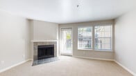 This single-floor residence offers a well-organized layout across several distinct living areas. The living room serves as the focal point of the home, highlighted by a classic fireplace with a slate tile surround and white mantel. Soft carpeting extends throughout the space, and large windows alongside a glass door flood the room with natural light and offer views of the surrounding greenery. The neutral, warm-toned walls create a clean and inviting atmosphere throughout.

The kitchen is equipped with dark espresso cabinetry, white countertops, and wood-look vinyl flooring. It includes a stainless steel dishwasher and accommodates in-unit washer and dryer units, adding everyday convenience. Adjacent areas provide additional counter space and storage.

The bedrooms are generously proportioned, each featuring plush carpeting, blinds-covered windows with natural views, and baseboard heating. One bedroom includes a large sliding-door closet, offering practical storage. Additional carpeted rooms with multiple windows provide flexibility for various uses.

Both bathrooms are finished with wood-look vinyl flooring, white tiled tub-shower combinations, and dark wood vanities topped with white countertops. One bathroom features a double-sink vanity with a large mirror and brushed nickel fixtures, lending a refined, functional feel to the space.