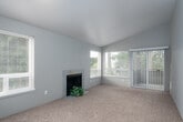 This single-floor residence offers a functional and comfortable layout designed with everyday living in mind. The spacious living room is a standout feature, showcasing vaulted ceilings, plush wall-to-wall carpeting, and a tiled fireplace flanked by large windows that flood the space with natural light. Sliding glass doors open to a private balcony overlooking mature greenery, creating a seamless indoor-outdoor connection.

Adjacent to the living area, a carpeted dining space connects to an open-concept kitchen via a convenient pass-through bar with seating. The kitchen is well-equipped with white upper cabinetry, grey lower cabinetry, granite-style countertops, stainless steel appliances including an electric range with overhead ventilation hood, and a refrigerator — offering both style and practicality.

The bedrooms are generously sized, each featuring plush carpeting and windows with blinds that allow for natural light while maintaining privacy. Neutral-toned walls throughout give the space a clean, cohesive feel.

The residence includes two bathrooms, both finished with grey cabinetry, granite-style countertops, and wood-look flooring. One bathroom features a shower-tub combo with a curtain, while the other offers a separate toilet room for added privacy. The overall ambiance is calm, bright, and move-in ready.