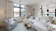 This thoughtfully designed two-bedroom, two-bathroom residence offers a contemporary living experience across a single floor. The open-concept layout connects the kitchen, dining, and living areas seamlessly, with light wood-style flooring flowing throughout the main living spaces. The kitchen is a standout feature, showcasing white gloss cabinetry, a subway tile backsplash, stainless steel appliances, and a large center island with quartz countertops and bar seating—ideal for both cooking and entertaining. The adjacent living area is bathed in natural light from oversized, floor-to-ceiling windows with outdoor views, creating a bright and airy atmosphere.

Both bedrooms are carpeted for comfort and feature large windows. The primary bedroom connects to a well-appointed en-suite bathroom, while the second bedroom offers convenient access to the second full bath. Both bathrooms are finished with striking chevron-patterned tile flooring, floating dark wood vanities, and clean white countertops, lending a modern, sophisticated aesthetic. Closet space is well-incorporated throughout. The overall design balances contemporary style with functional living in a cohesive, neutral palette.