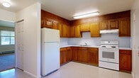 This two-story home distributes its living space efficiently across two floors, with the ground level housing the kitchen and primary living areas, while the upper floor accommodates the bedrooms. The kitchen features warm oak cabinetry extending to the ceiling, offering generous storage, white appliances including a refrigerator and electric range, and light tile flooring. A window provides natural light and an outdoor view, while a baseboard heating unit ensures year-round comfort. An electrical panel is conveniently accessible nearby.

The bedrooms are carpeted and feature neutral walls, creating a calm, functional atmosphere. Upper-floor bedrooms showcase angled rooflines with sloped ceilings that add architectural character, along with windows that draw in natural light. Each bedroom includes its own closet, with at least one featuring a double sliding-door closet for added storage. The primary bedroom offers a comfortable, generously sized layout.

The bathroom is clean and straightforward, featuring a tiled tub-shower combination, a vanity with storage, a toilet, and marble-patterned tile flooring. Two staircases connect the floors, facilitating smooth circulation throughout the home.
