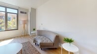 This thoughtfully designed single-floor unit offers a clean, modern aesthetic throughout, characterized by light wood flooring, crisp white walls, and an abundance of natural light. The open-concept layout seamlessly connects the living and sleeping areas, with a low half-wall providing a subtle sense of separation while maintaining an airy, spacious feel.

The kitchen is a standout feature, outfitted with contemporary two-tone cabinetry, dark stone countertops, stainless steel appliances including a gas range, built-in microwave, and dishwasher, as well as a textured tile backsplash. A large window floods the kitchen with natural light and offers pleasant outdoor views.

The living area is defined by its relaxed, minimalist character, with warm-toned area rugs and a curved tufted sofa that adds a stylish focal point. The sleeping area is comfortably appointed and includes a generously sized sliding-door closet with built-in hanging storage.

The bathroom features tile flooring, a full soaking tub with a tiled surround, a dark-countered vanity with modern cabinetry, and clean, functional fixtures. Throughout the unit, the consistent use of neutral tones and modern finishes creates a cohesive and inviting atmosphere well-suited for comfortable everyday living.