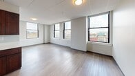 Located at 455 Main St in the heart of downtown Worcester, Massachusetts, this single-floor unit offers a thoughtfully designed open layout with a clean, modern aesthetic throughout. Light-toned hardwood-style flooring runs continuously across the space, providing a cohesive and contemporary feel.

The kitchen is a functional centerpiece, featuring rich dark-wood cabinetry, light countertops, and stainless steel appliances including a refrigerator and microwave. A peninsula counter creates a natural division between the kitchen and the expansive open living area, which benefits from a drop-panel ceiling with flush-mount lighting.

The living space is generously sized and bathed in natural light from large black-framed windows that frame striking views of the Worcester cityscape, including the surrounding urban architecture and skyline. Multiple windows across different rooms ensure excellent light penetration throughout the unit.

The bedroom is a well-proportioned, quiet retreat with its own set of large windows overlooking the city. The bathroom is efficiently designed with a vanity featuring a dark cabinet base, a wall-mounted mirror, and a full tub-shower combination with chrome fixtures.

The unit's urban location and elevated vantage point make it a compelling option for those seeking a modern residence with direct access to downtown Worcester's amenities and city energy.