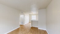 This single-story, 2-bedroom, 1-bathroom unit offers a practical and cohesive layout designed for comfortable everyday living. Wood-look tile flooring runs throughout the home, providing a warm, consistent aesthetic across every room. Textured ceilings add a subtle architectural detail visible in the living room and bedrooms alike.

The living room is a bright, open space anchored by a large window that invites ample natural light. A partial countertop divider separates it from the kitchen, which features warm oak cabinetry, a double-basin sink, white appliances, and a window above the counter. A door in the kitchen provides direct exterior access.

Both bedrooms are well-proportioned and naturally lit, each featuring windows with blinds that allow for flexible light control. The primary bedroom includes a closet with a paneled door. The second bedroom is similarly bright, with a wide window offering outdoor views.

The bathroom is appointed with a full tub-and-shower combination. The surround features marble-style tile paired with a decorative mosaic accent band in multicolor tones, lending a polished look. A window above the tub adds natural light to the space.

A hallway connects the main areas efficiently, completing this straightforward and well-maintained single-floor layout.