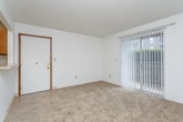 This single-floor unit offers a straightforward, functional layout designed to maximize usable living space. The open living area is finished with neutral-toned wall-to-wall carpeting and crisp white walls, creating a clean and versatile backdrop. A textured ceiling runs throughout the main living spaces, adding subtle dimension overhead. A ceiling fan is installed in a secondary area just off the main living room, enhancing airflow and comfort.

The kitchen is configured in a galley style, featuring warm wood-toned cabinetry, light countertops, tile flooring, and white appliances including a refrigerator and range. A dishwasher is also included. The kitchen connects to the living area via a pass-through opening, promoting an open feel while maintaining defined zones. An entry door with a brass-toned hardware detail is positioned adjacent to the kitchen pass-through.

The living room benefits from a large sliding glass door dressed with vertical blinds, allowing ample natural light and providing access to an outdoor area. The bedrooms are carpeted and offer adequate space, with one featuring a high-set window for privacy. The bathroom includes tile flooring, a wood-tone vanity with a light countertop, and a separate tub and shower area.