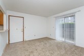 This single-floor unit offers a straightforward, functional layout designed to maximize usable living space. The open living area is finished with neutral-toned wall-to-wall carpeting and crisp white walls, creating a clean and versatile backdrop. A textured ceiling runs throughout the main living spaces, adding subtle dimension overhead. A ceiling fan is installed in a secondary area just off the main living room, enhancing airflow and comfort.

The kitchen is configured in a galley style, featuring warm wood-toned cabinetry, light countertops, tile flooring, and white appliances including a refrigerator and range. A dishwasher is also included. The kitchen connects to the living area via a pass-through opening, promoting an open feel while maintaining defined zones. An entry door with a brass-toned hardware detail is positioned adjacent to the kitchen pass-through.

The living room benefits from a large sliding glass door dressed with vertical blinds, allowing ample natural light and providing access to an outdoor area. The bedrooms are carpeted and offer adequate space, with one featuring a high-set window for privacy. The bathroom includes tile flooring, a wood-tone vanity with a light countertop, and a separate tub and shower area.