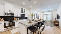 This single-floor residence showcases a thoughtfully designed open-concept layout that seamlessly connects the kitchen, dining, and living areas. The kitchen is a standout feature, outfitted with crisp white shaker cabinetry, glass-front upper cabinets, and a striking black hexagonal tile backsplash. A generously sized granite-topped island with built-in shelving provides seating for multiple bar stools, making it an ideal space for casual dining and entertaining. Stainless steel appliances and a farmhouse sink complete the functional design.

The living area is bright and welcoming, benefiting from natural light streaming through French doors fitted with plantation shutters and transom windows. Light hardwood flooring flows consistently throughout the space, reinforcing a cohesive aesthetic.

The bedrooms are well-proportioned and serene, each offering access to natural light. The primary suite includes a spacious walk-in closet with wire shelving and a refined en-suite bathroom featuring dual granite-topped vanities, LED-backlit mirrors with black hardware accents, and tile flooring. A secondary bedroom provides a comfortable and well-lit retreat. The overall ambiance is modern and clean, with a neutral palette punctuated by warm wood tones.
