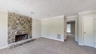 This single-floor, 1-bedroom, 1-bathroom residence offers a thoughtfully organized layout across a comfortable footprint. The living room serves as the centerpiece of the home, highlighted by a dramatic floor-to-ceiling stone fireplace with a raised hearth that adds character and warmth to the space. Soft carpeting, crown molding, and a textured ceiling contribute to a cozy yet polished atmosphere. Natural light filters in through multiple windows and a glass-panel exterior door that leads to an outdoor area. The kitchen is a functional galley-style space featuring gray cabinetry, light countertops, hardwood-style flooring, and black appliances including a range and refrigerator, all accented by crown molding for a finished look. The spacious primary bedroom offers ample room and direct outdoor access through a glass door framed by a window, allowing for generous natural light and views of surrounding greenery. The bathroom includes a wide vanity with light countertops, gray cabinetry, a large mirror, and a combined tub and shower. A dedicated laundry area with washer and dryer hookups and hardwood-style flooring adds everyday convenience, completing this well-appointed residence.