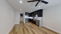 This thoughtfully designed single-floor unit makes efficient use of its space through an open-concept layout that seamlessly integrates the kitchen and living area. Light oak hardwood flooring runs throughout, creating a warm and cohesive aesthetic complemented by crisp white walls and recessed lighting.

The kitchen is a standout feature, showcasing floor-to-ceiling dark espresso shaker cabinets that contrast boldly against a speckled granite countertop and a mosaic tile backsplash. A stainless steel farmhouse sink, full suite of stainless steel appliances — including a side-by-side refrigerator, electric range, and dishwasher — and a under-cabinet range hood complete the well-equipped cooking space. The living area, adjacent to the kitchen, benefits from a ceiling fan with recessed lighting above and a window that invites natural light through the room.

A hallway connects the main living space to the bathroom, which is finished with white subway tile wainscoting, dark slate floor tile, a dark-cabinet vanity topped with granite, a framed mirror, and a frosted window for privacy and natural light. The overall ambiance of the unit is modern and clean, with a consistent design language of dark cabinetry, granite surfaces, and light wood flooring tying every room together.