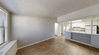 This single-story 1-bedroom unit offers a practical and cohesive layout with wood-look flooring extending throughout every room, tying the space together with a warm, consistent aesthetic. Neutral gray walls and white trim complement the textured ceilings, creating a clean and understated backdrop.

The living area is generously proportioned, providing ample room for furnishing arrangements. Natural light enters through a window near the front entry door, brightening the open space. The layout connects the living area directly to the kitchen, which is separated by a half-wall partition with open shelving below. The kitchen features white cabinetry with brushed nickel hardware, stone-patterned countertops, a stainless steel sink, and white appliances including an electric range with overhead ventilation.

The bedroom is a comfortable, well-sized room equipped with a ceiling fan with light fixture and a window that allows natural light. The full bathroom includes a tub/shower combination, a white vanity with stone-patterned countertop, and wood-look tile flooring. A dedicated laundry room accommodates a full-size washer and dryer, adding everyday convenience to the unit.