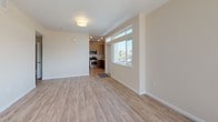 This 2-bedroom, 2-bathroom single-floor residence offers a thoughtfully designed layout with contemporary finishes throughout. The open living area is bathed in natural light streaming through large windows, complemented by light wood-style flooring that extends seamlessly across the main living spaces. The kitchen is equipped with stainless steel appliances, including a gas range and microwave, set against warm wood cabinetry, tile backsplash, and crisp white countertops. A window above the sink provides pleasant outdoor views of the surrounding neighborhood. The entry foyer features transom windows that bring in additional natural light, creating a bright and welcoming arrival experience. Both bedrooms are carpeted for comfort and receive ample daylight through well-placed windows with views of the surrounding area. The primary bathroom features a dual-sink vanity with dark wood cabinetry, a large mirror, and wood-style flooring, with a separate carpeted walk-in area adjacent. The second bathroom includes a single-sink vanity with matching cabinetry, a full tub-shower combination, and a large mirror. Both bathrooms are finished with clean, neutral tones and modern fixtures. The overall design emphasizes a clean, modern aesthetic with neutral walls and consistent flooring materials throughout.