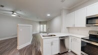 Located at 2430 Cheshire Bridge Rd NE in Atlanta, GA, this well-appointed single-floor unit offers a thoughtfully designed open-concept layout that maximizes every inch of available space. The combined kitchen and living area serves as the heart of the unit, finished with warm-toned wood-look flooring and neutral gray walls accented by crisp crown molding throughout.

The kitchen is a standout feature, centered around a white peninsula with a stainless steel undermount sink and sleek white quartz-style countertops. White shaker-style cabinetry lines the walls, providing ample storage, while a full suite of stainless steel appliances — including a refrigerator, electric range, over-the-range microwave, and dishwasher — ensures modern functionality. Recessed lighting illuminates the workspace effectively.

The living area benefits from natural light streaming through a set of glass French doors, creating a bright and welcoming atmosphere. The open layout allows for flexible furniture arrangements, making the space feel airy and versatile.

The bathroom is clean and well-finished, featuring a full soaking tub with a tiled surround, chrome fixtures, and a vanity with ample counter space. A dedicated walk-in closet with wire shelving provides practical storage solutions. The consistent flooring and neutral color palette throughout the unit create a cohesive, modern aesthetic.