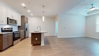 Located at 5380 Desoto Rd in Sarasota, Florida, this single-story residence showcases a contemporary design with clean lines, light-toned luxury vinyl plank flooring, and a bright, neutral color palette throughout. The open-concept kitchen serves as the heart of the home, featuring a central island with granite countertops, pendant lighting, and a built-in sink. Two-tone cabinetry—combining white upper cabinets with warm wood-toned lower cabinets—pairs with a subway tile backsplash and a full suite of stainless steel appliances, including a side-by-side refrigerator with ice maker, electric range, and microwave. The kitchen flows seamlessly into a generous living area equipped with a ceiling fan and abundant natural light from multiple windows. The bedrooms offer a comfortable retreat; one features plush carpeting, a tray ceiling, and a wide window framing natural views, while another includes wood-look flooring and a ceiling fan. A well-designed bathroom includes a glass-enclosed walk-in shower with large-format tile, granite vanity, and wood-toned cabinetry. A dedicated hallway area provides in-unit laundry. Throughout the home, recessed lighting, crisp white walls, and thoughtful finishes create a polished, move-in-ready atmosphere.