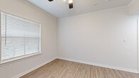 Located at 200 Kellington Dr N in Houston, TX, this single-floor, 2-bedroom, 2-bathroom home offers a clean, modern aesthetic throughout. Light-toned wood-look flooring flows through the main living areas and kitchen, complemented by crisp white walls, crown molding, and bold matte-black hardware accents that add a contemporary touch.

The kitchen is a standout feature, boasting white shaker-style cabinetry, light stone countertops, a deep stainless steel sink, and stainless steel appliances including a range, microwave, and refrigerator. A peninsula with pendant lighting connects the kitchen to the dining and living area, creating an open, functional layout.

The primary bedroom offers a comfortable retreat with a ceiling fan, natural light from a window with blinds, and hardwood-style flooring. The second bedroom features plush carpeting, a ceiling fan, and a glass-panel door that opens to the outdoors, bringing in additional natural light and views of the greenery beyond.

Both bathrooms are finished with wood-look tile flooring, white vanities with ample storage, and matte-black fixtures. A practical bonus is the in-unit stacked washer and dryer tucked neatly into one of the bathrooms, alongside wire shelving for added storage. A dedicated closet provides further organization. The home presents a fresh, move-in-ready feel throughout.