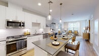 This single-floor residence offers a thoughtfully designed open-concept layout that seamlessly connects the kitchen, dining, and living areas. The kitchen is outfitted with crisp white shaker cabinetry extending to the ceiling, a classic subway tile backsplash, dark quartz countertops, and a full suite of stainless steel appliances including a gas range, built-in microwave, dishwasher, and refrigerator. A spacious island with pendant lighting serves as both a prep space and casual dining area. Light wood-style flooring runs throughout the main living areas, enhancing the bright and airy atmosphere. The living room benefits from large windows that invite natural light and offer views of the surrounding greenery. Both bedrooms are carpeted and feature generous windows, neutral tones, and a calm, restful ambiance. The primary bedroom is complemented by a dedicated walk-in closet with open shelving and hanging storage. The full bathroom is clean and modern, featuring tile surround, a soaking tub with shower, a dark-cabinet vanity, and light flooring. Overall, the space presents a cohesive, contemporary aesthetic with a neutral palette accented by warm and natural tones.