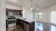 Located at 7035 Pickwell Dr in San Antonio, TX, this single-story, one-bedroom, one-bathroom unit offers a thoughtfully designed layout with quality finishes throughout. The open-concept kitchen is a standout feature, equipped with dark espresso cabinetry, stainless steel appliances — including an electric range and microwave — granite countertops, a tile backsplash, and a peninsula with a stainless steel sink that opens to the living area. Polished concrete floors run through the kitchen, living, and bathroom areas, lending a sleek, modern aesthetic. The bedroom is carpeted for comfort, features a ceiling fan, and receives natural light through a window overlooking the greenery outside. The bathroom is efficiently laid out with a glass-enclosed walk-in shower, granite vanity countertop, dark wood cabinetry, and matching polished concrete floors. A hallway connects the main living spaces, and the entrance provides a clean transition into the home. The covered outdoor patio area is bordered by mature trees and fencing, offering a natural, private backdrop. The unit's cohesive design — anchored by granite surfaces, dark wood finishes, and polished concrete — presents a clean, contemporary living environment.