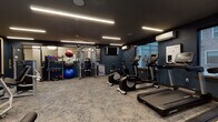 Located at 44 Veterans Memorial Drive in Somerville, New Jersey, this fitness center is a thoughtfully designed, single-floor facility that offers a comprehensive range of exercise equipment and amenities. The space is defined by its bold navy blue walls, dark ceiling, and patterned carpet flooring, creating a sleek, modern aesthetic that feels both energizing and focused.

Linear LED strip lighting runs across the ceiling, providing consistent, even illumination throughout the space. A ceiling fan adds ventilation support, while wall-mounted air conditioning units ensure climate control year-round. Large windows along one wall allow natural light to filter in and offer views of the surrounding outdoor greenery, lending the space an open quality despite its interior setting.

The cardio zone is well-stocked with multiple treadmills, ellipticals, a stair climber, and stationary bikes, including both upright and recumbent options, all from Life Fitness. A dedicated strength and functional training area features a multi-use cable machine, adjustable benches, and an assortment of kettlebells and stability balls organized on wall-mounted racks. A large framed mirror spans one wall, enhancing the sense of space while supporting proper form during workouts. Wall-mounted televisions are positioned for visibility throughout, completing the facility's practical and polished design.