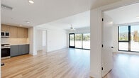 This thoughtfully designed single-floor unit offers a bright and contemporary living experience across eight rooms. The open living and dining area is anchored by light hardwood flooring and crisp white walls, with a ceiling fan overhead and expansive floor-to-ceiling sliding glass doors that lead to a private balcony, flooding the space with natural light and framing scenic outdoor views of the surrounding neighborhood.

The modern kitchen is well-appointed with a two-tone cabinetry scheme — light wood upper cabinets paired with muted blue-grey lower cabinets — set against clean white countertops and a seamless backsplash. Stainless steel appliances, including a gas range, built-in microwave, and refrigerator, complete the functional and stylish culinary space.

The bedrooms maintain the clean, minimalist aesthetic with white walls and continuous hardwood flooring. A spacious walk-in closet with built-in shelving and hanging rods provides generous storage. Two full bathrooms are finished with large-format tile, soaking tubs with tiled surrounds, light wood vanities, stone-topped counters, undermount sinks, and sleek matte black fixtures throughout. The overall design is cohesive, modern, and move-in ready.