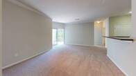Located at 1000 Presidents Way in Dedham, Massachusetts, this single-floor residence offers a well-organized layout designed for comfortable everyday living. The open living area is finished with plush wall-to-wall carpeting and features crown molding, track lighting, and a sliding glass door that leads to a private balcony with outdoor views of surrounding greenery. A half-wall peninsula separates the living space from the kitchen, which is configured in a galley style with warm wood cabinetry, dark granite-style countertops, and black appliances including a range, microwave, and dishwasher. Light wood-style flooring runs throughout the kitchen and continues into an adjoining utility area with bifold doors. The bedrooms are carpeted and bright, with large double-pane windows that invite natural light and frame views of the tree-lined surroundings. The bathrooms are finished with wood-style flooring, rich cherry-toned cabinetry, dark countertops, and white tiled tub/shower combinations with chrome fixtures. Clean neutral walls and consistent finishes throughout the unit create a cohesive and functional aesthetic. The overall design emphasizes practicality and comfort, with thoughtful details that enhance the livability of the space.