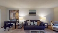 This single-floor residence offers a thoughtfully designed layout that balances comfort and functionality across its key living spaces. The kitchen is outfitted with warm honey-toned wood cabinetry, light speckled countertops, and a full suite of stainless steel appliances including a refrigerator, electric range with microwave above, and dishwasher. Wood-look flooring runs throughout the kitchen and dining areas, adding a cohesive, warm aesthetic. The dining area sits just off the entryway, accented by a ceiling light fixture and a built-in coat closet for added convenience. The living room is generously sized, featuring plush carpeting and a corner arrangement of large windows that invite abundant natural light and views of lush greenery outside. Two well-proportioned bedrooms each include windows with outdoor views, carpeted floors, and baseboard heating. The bathrooms are finished with wood-look flooring, light countertops, and tub-shower combinations. One bathroom notably features an in-unit stacked washer and dryer tucked within a dedicated closet, offering practical laundry access. Throughout the space, textured ceilings and neutral wall tones create a clean, inviting atmosphere suited for everyday living.